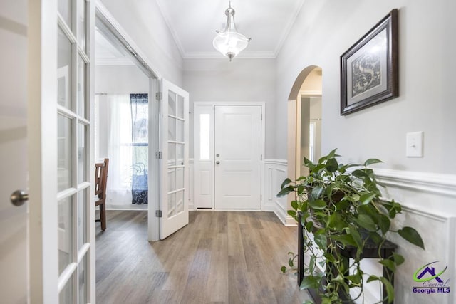 entrance foyer with crown molding, arched walkways, french doors, and light wood finished floors
