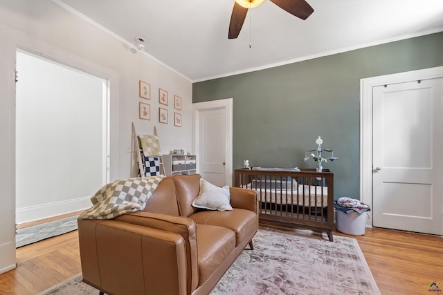 bedroom featuring crown molding, a nursery area, ceiling fan, and wood finished floors