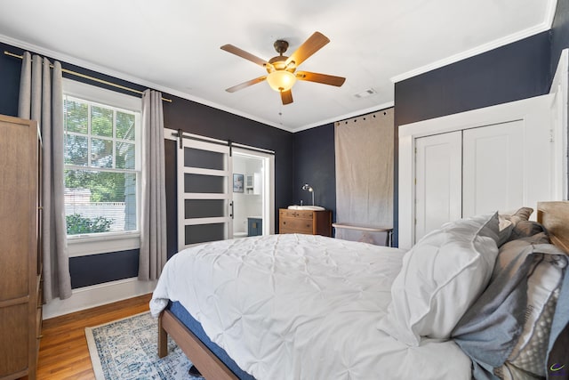 bedroom featuring crown molding, a barn door, wood finished floors, and visible vents