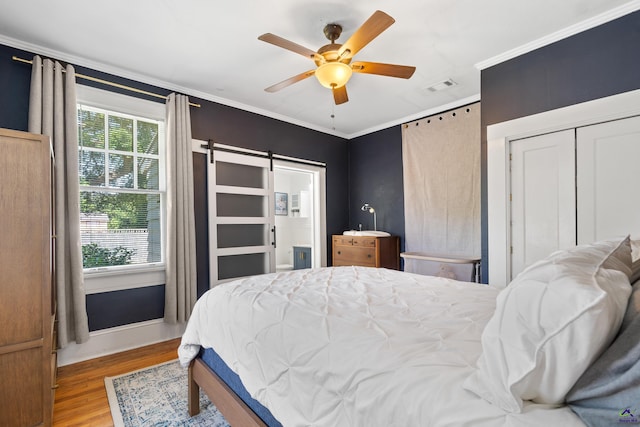 bedroom featuring a barn door, crown molding, wood finished floors, and visible vents