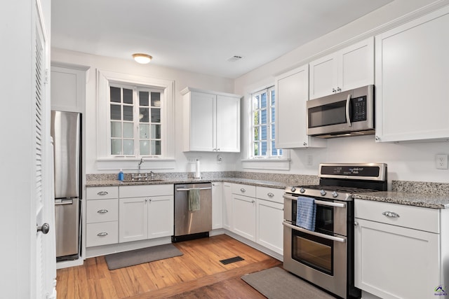 kitchen with light stone countertops, a sink, light wood-style flooring, stainless steel appliances, and white cabinetry