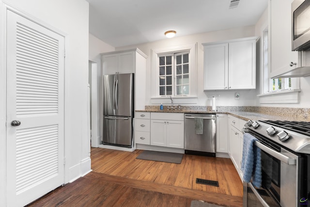 kitchen with visible vents, appliances with stainless steel finishes, light wood-type flooring, light stone counters, and white cabinets