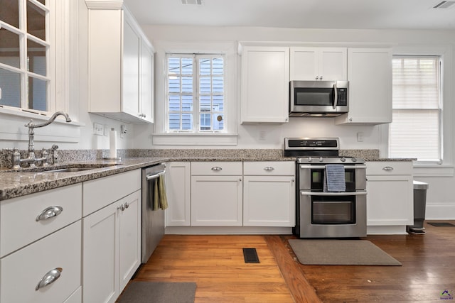 kitchen with light wood-style flooring, white cabinets, a sink, stone counters, and stainless steel appliances
