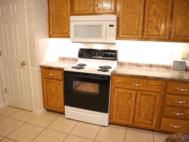 kitchen featuring brown cabinets, light tile patterned floors, range with electric stovetop, and white microwave
