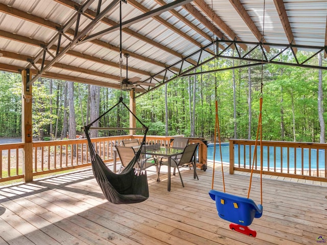 wooden deck with a forest view, ceiling fan, and outdoor dining area