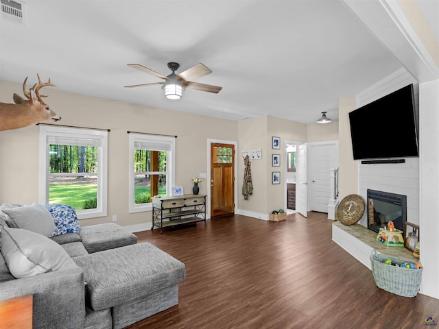 living area featuring dark wood finished floors, a large fireplace, a ceiling fan, baseboards, and visible vents