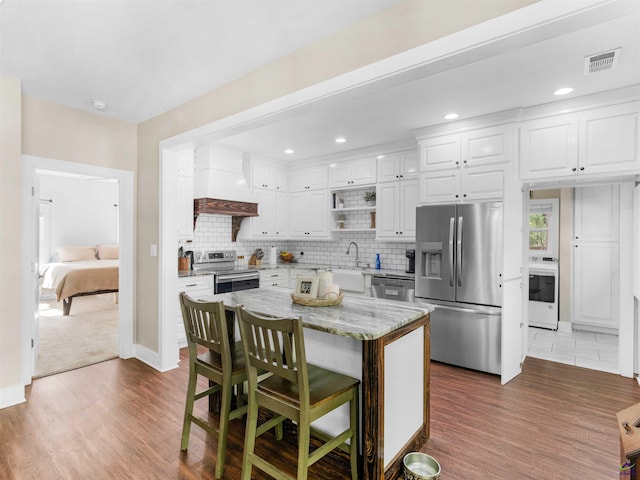 kitchen with appliances with stainless steel finishes, premium range hood, dark wood-style flooring, and visible vents