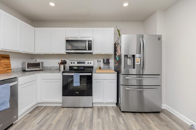 kitchen featuring stainless steel appliances, light wood-type flooring, white cabinetry, and a toaster