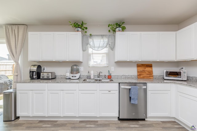 kitchen with a sink, light stone counters, white cabinets, and stainless steel dishwasher