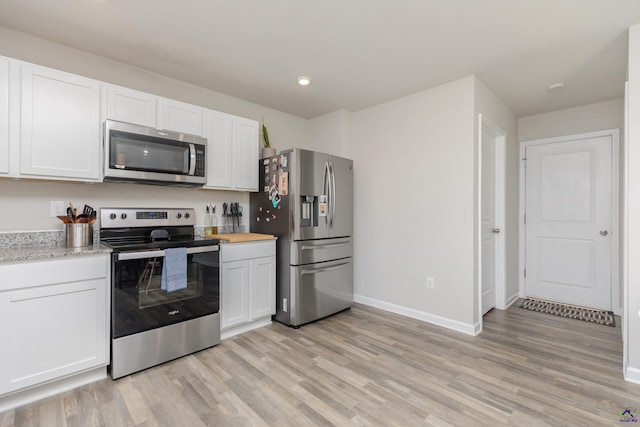 kitchen with white cabinets, baseboards, appliances with stainless steel finishes, and light wood-type flooring