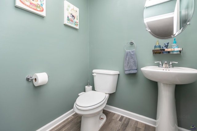 half bath with toilet, baseboards, a sink, and wood finished floors