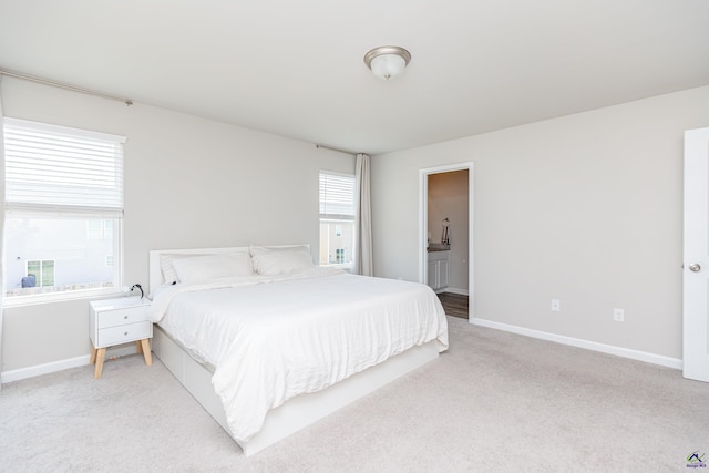 bedroom featuring baseboards, multiple windows, ensuite bathroom, and light colored carpet