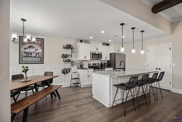 kitchen featuring appliances with stainless steel finishes, an inviting chandelier, a breakfast bar area, white cabinetry, and a center island with sink