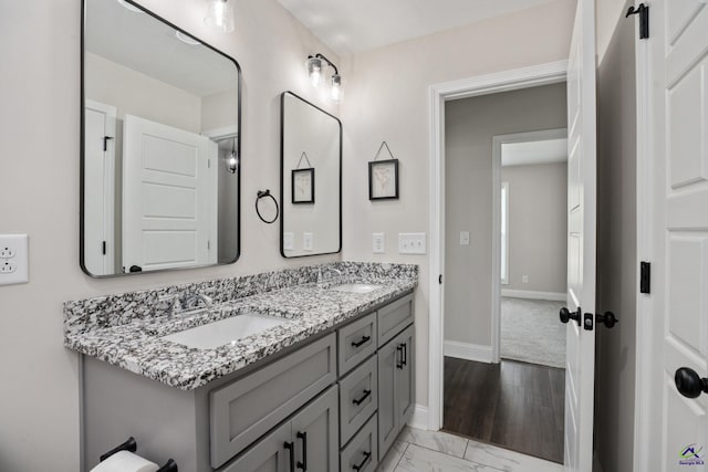 bathroom with baseboards, a sink, marble finish floor, and double vanity