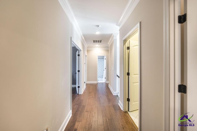 hall with dark wood-style floors, baseboards, visible vents, and ornamental molding