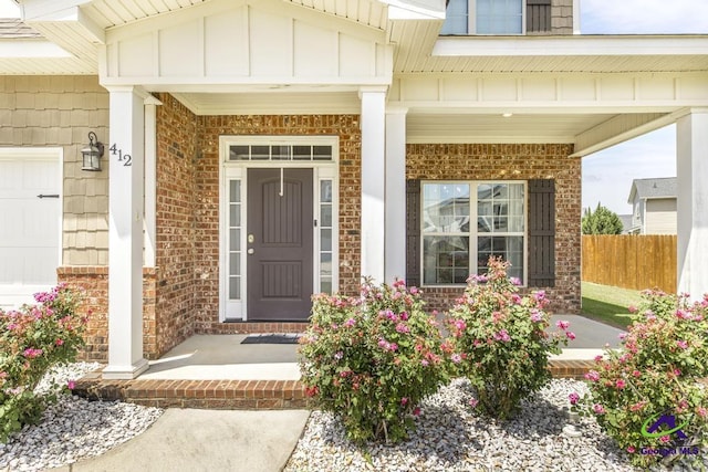 view of exterior entry featuring covered porch, brick siding, board and batten siding, and fence