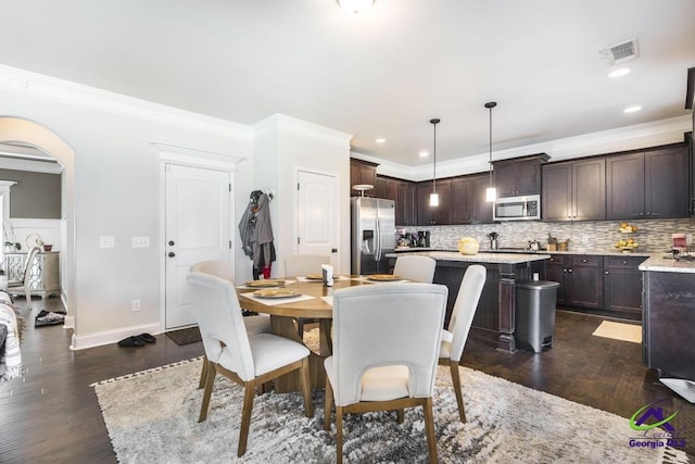 dining area with visible vents, arched walkways, dark wood-style flooring, and crown molding