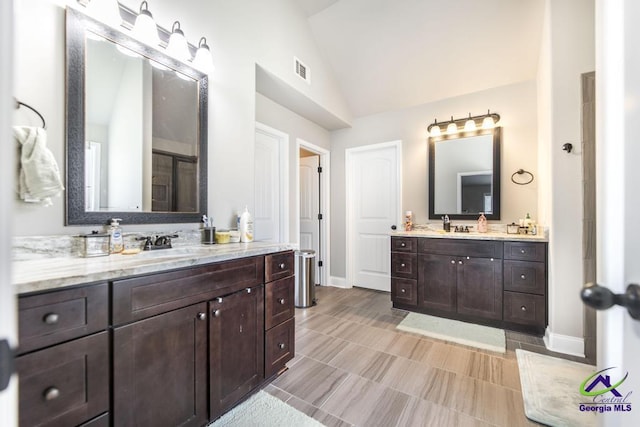 full bathroom with visible vents, baseboards, two vanities, a sink, and vaulted ceiling