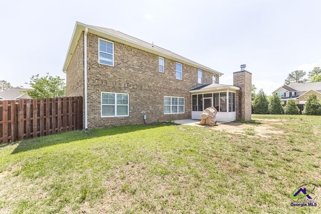 back of property featuring fence, a chimney, a sunroom, brick siding, and a lawn