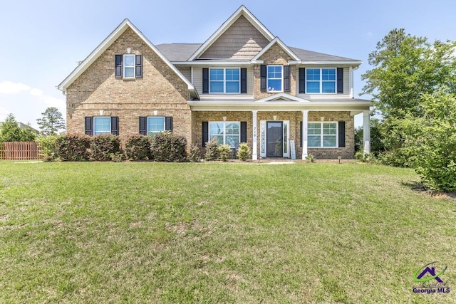 craftsman-style house with covered porch, brick siding, fence, and a front lawn
