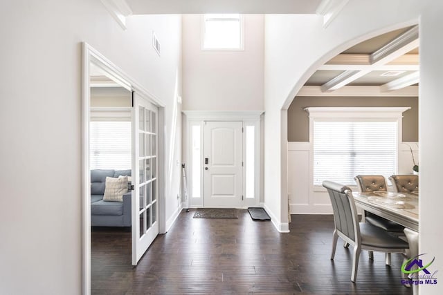 foyer featuring visible vents, ornamental molding, beamed ceiling, arched walkways, and dark wood finished floors