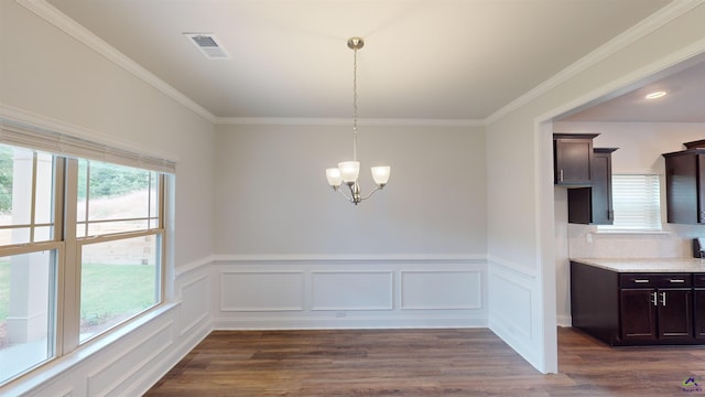 unfurnished dining area with visible vents, crown molding, dark wood finished floors, a wainscoted wall, and an inviting chandelier