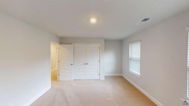 unfurnished bedroom featuring a closet, baseboards, light colored carpet, and visible vents