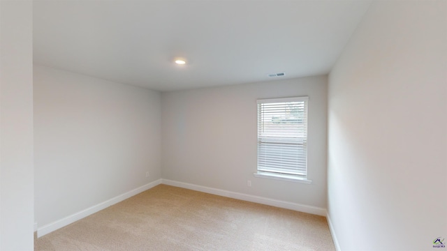 spare room featuring baseboards, light colored carpet, and visible vents