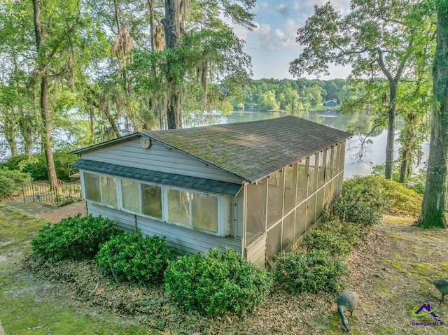 view of property exterior with a shingled roof, a water view, and a sunroom