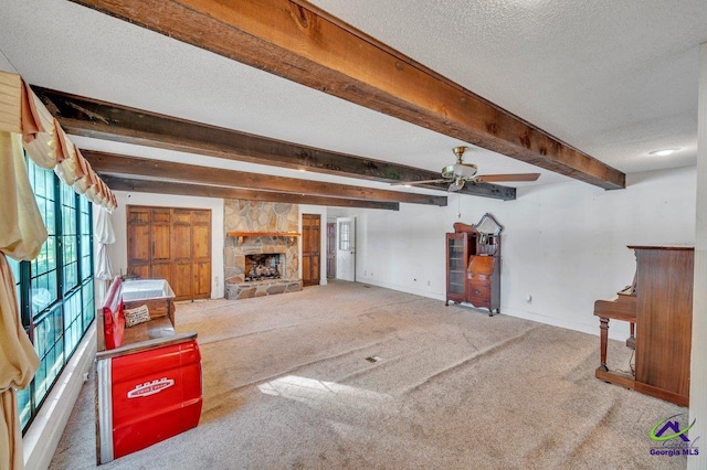 unfurnished living room with ceiling fan, carpet floors, a stone fireplace, baseboards, and beamed ceiling