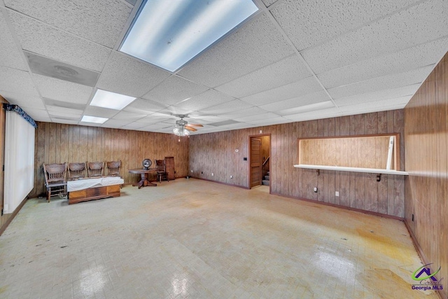 unfurnished room with wooden walls, ceiling fan, and a drop ceiling