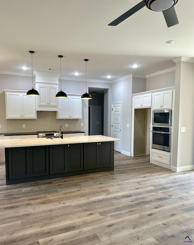 kitchen with a ceiling fan, stainless steel appliances, a large island with sink, and white cabinetry