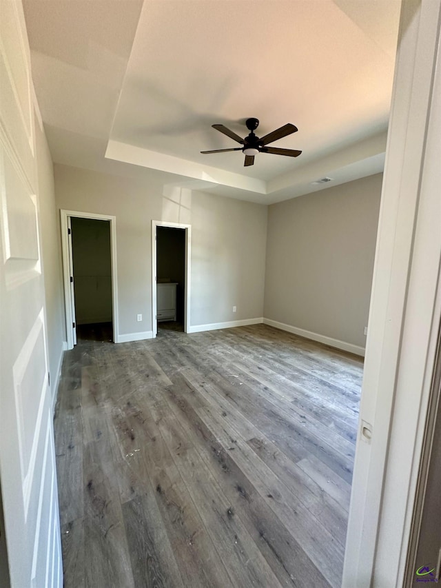 unfurnished bedroom with visible vents, wood finished floors, baseboards, ceiling fan, and a raised ceiling