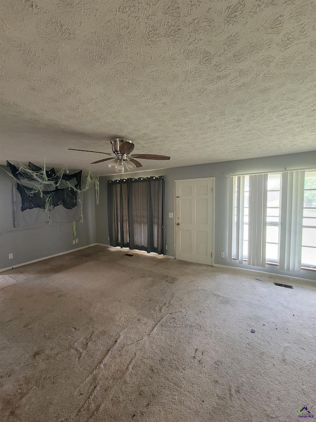 empty room featuring visible vents, a ceiling fan, baseboards, a textured ceiling, and carpet flooring