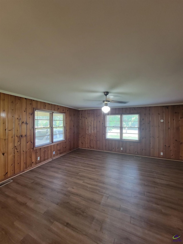 empty room featuring plenty of natural light, dark wood-style flooring, ceiling fan, and visible vents