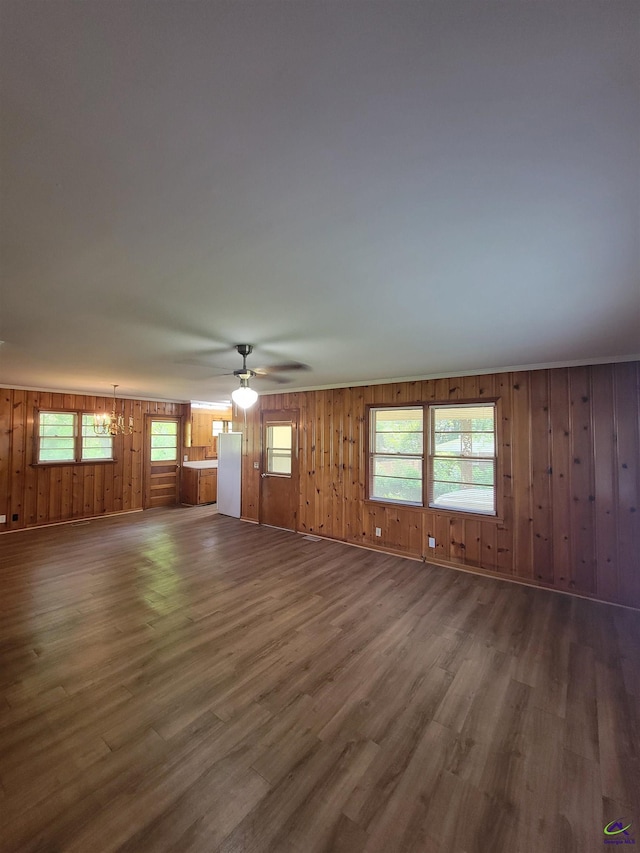 unfurnished living room with a healthy amount of sunlight, ceiling fan, wooden walls, and wood finished floors