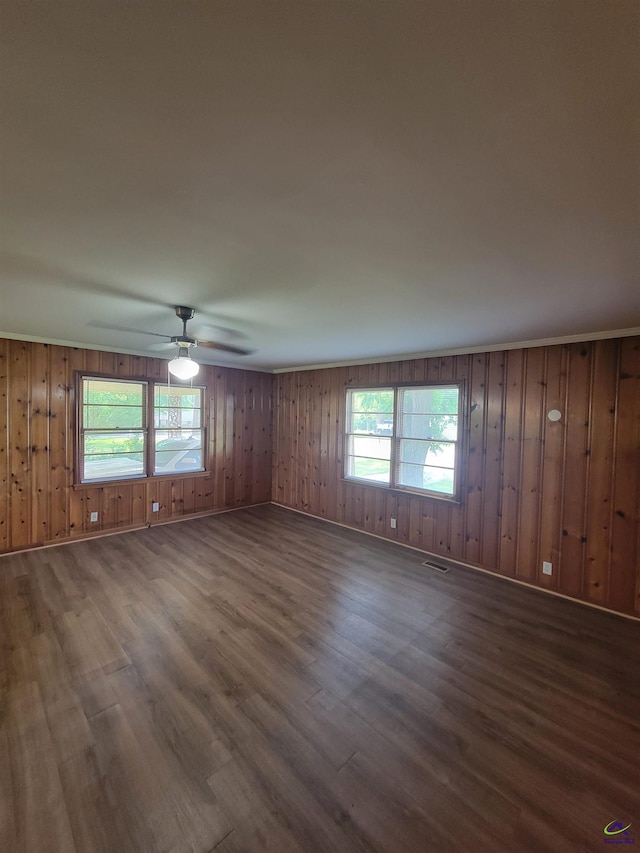 spare room with visible vents, wood walls, wood finished floors, baseboards, and a ceiling fan