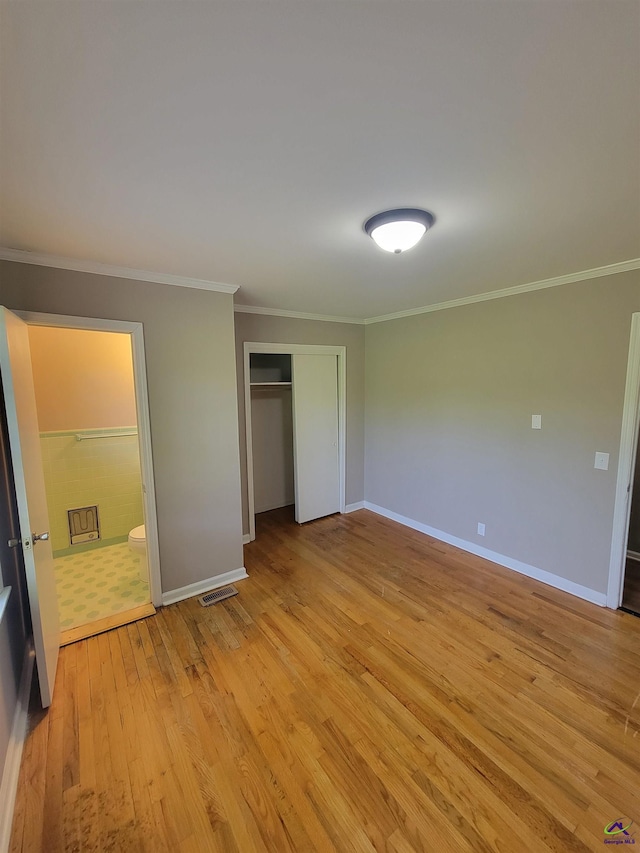 unfurnished bedroom featuring a closet, baseboards, ornamental molding, and light wood-style floors