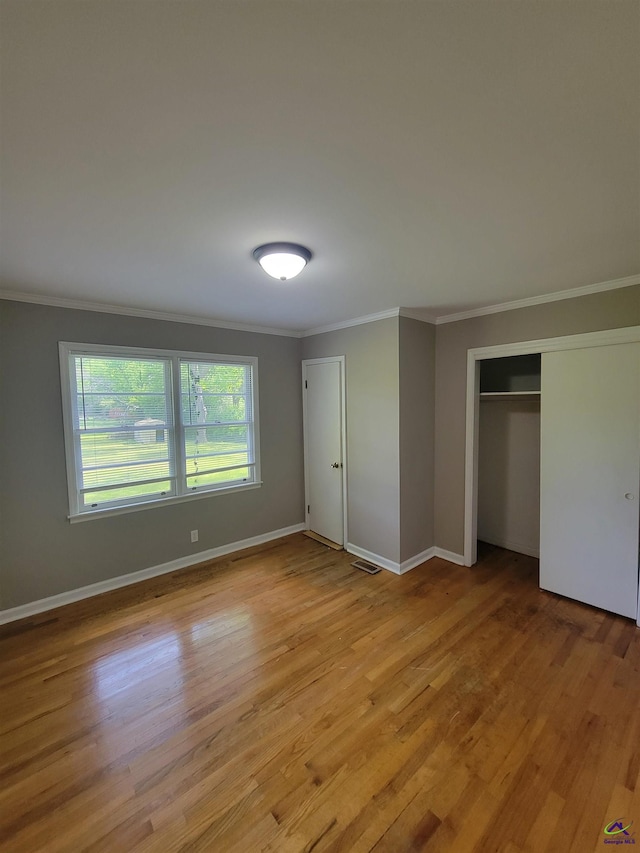 unfurnished bedroom featuring crown molding, light wood-style floors, baseboards, visible vents, and a closet