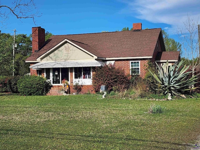 view of front facade featuring entry steps, a chimney, brick siding, and a front yard