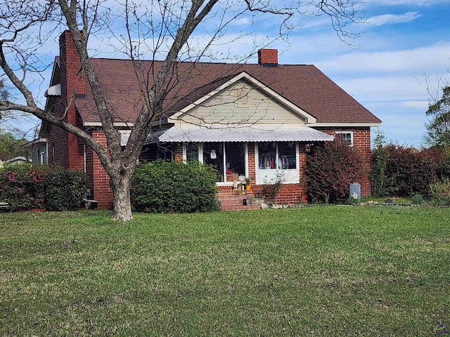 bungalow featuring brick siding, roof with shingles, a front yard, and a chimney
