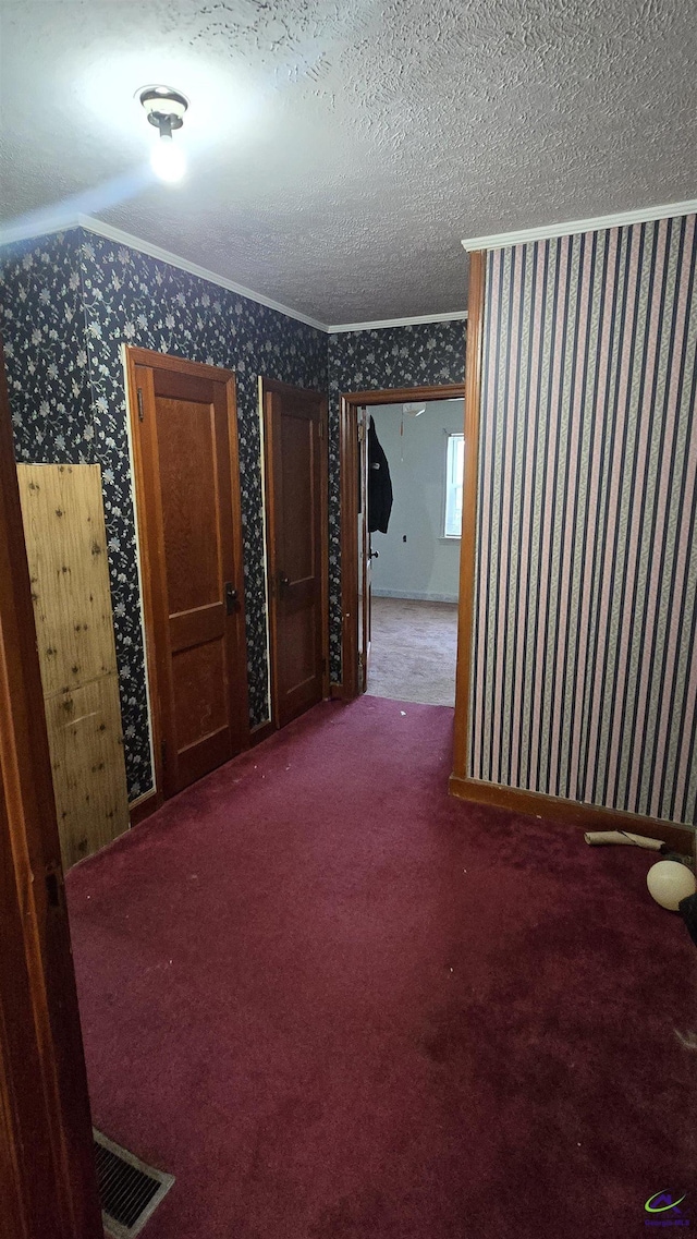 empty room featuring crown molding, carpet flooring, a textured ceiling, wallpapered walls, and visible vents