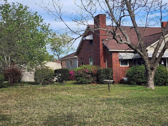view of home's exterior with a yard, brick siding, a chimney, and roof with shingles