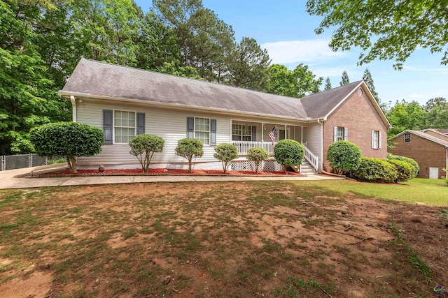 single story home featuring fence, a porch, roof with shingles, and a front yard