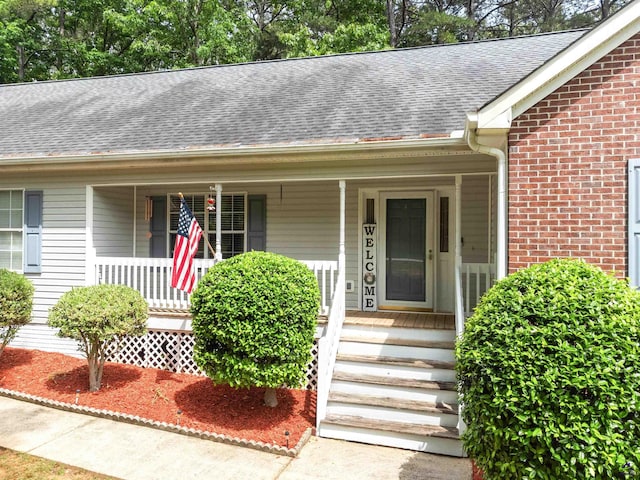 property entrance with covered porch, brick siding, and a shingled roof