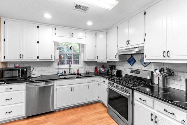 kitchen with visible vents, appliances with stainless steel finishes, dark countertops, a sink, and under cabinet range hood