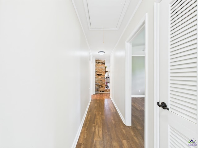 hallway featuring baseboards, attic access, wood finished floors, and ornamental molding