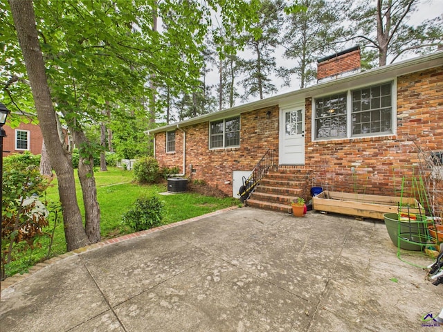 ranch-style house with a front lawn, a chimney, brick siding, entry steps, and central air condition unit