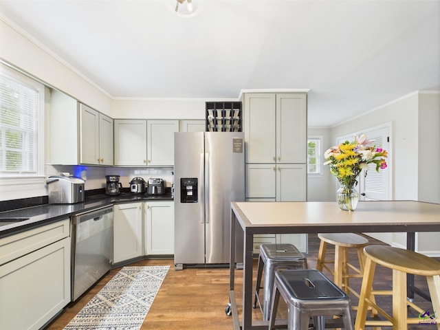 kitchen with decorative backsplash, dark countertops, wood finished floors, ornamental molding, and stainless steel appliances
