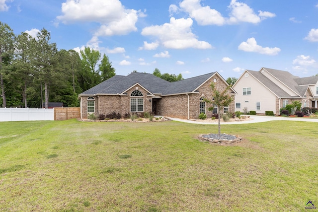 ranch-style home featuring brick siding, fence, and a front lawn